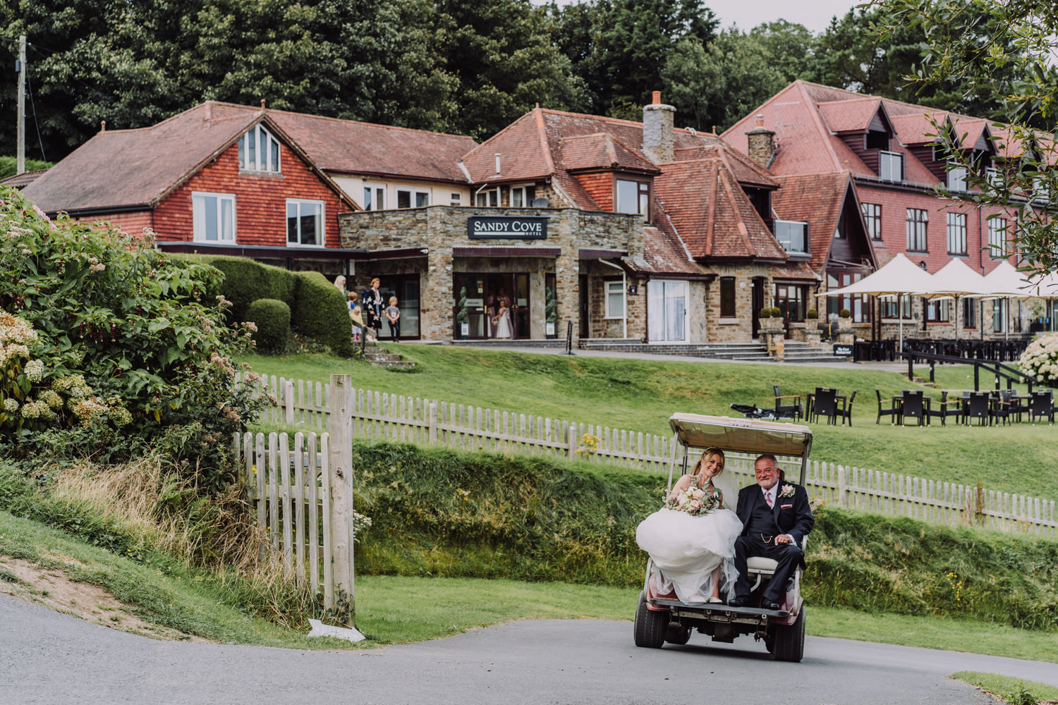 sandy cove wedding in north devon, bride and father being escorted to ceremony in a golf buggy