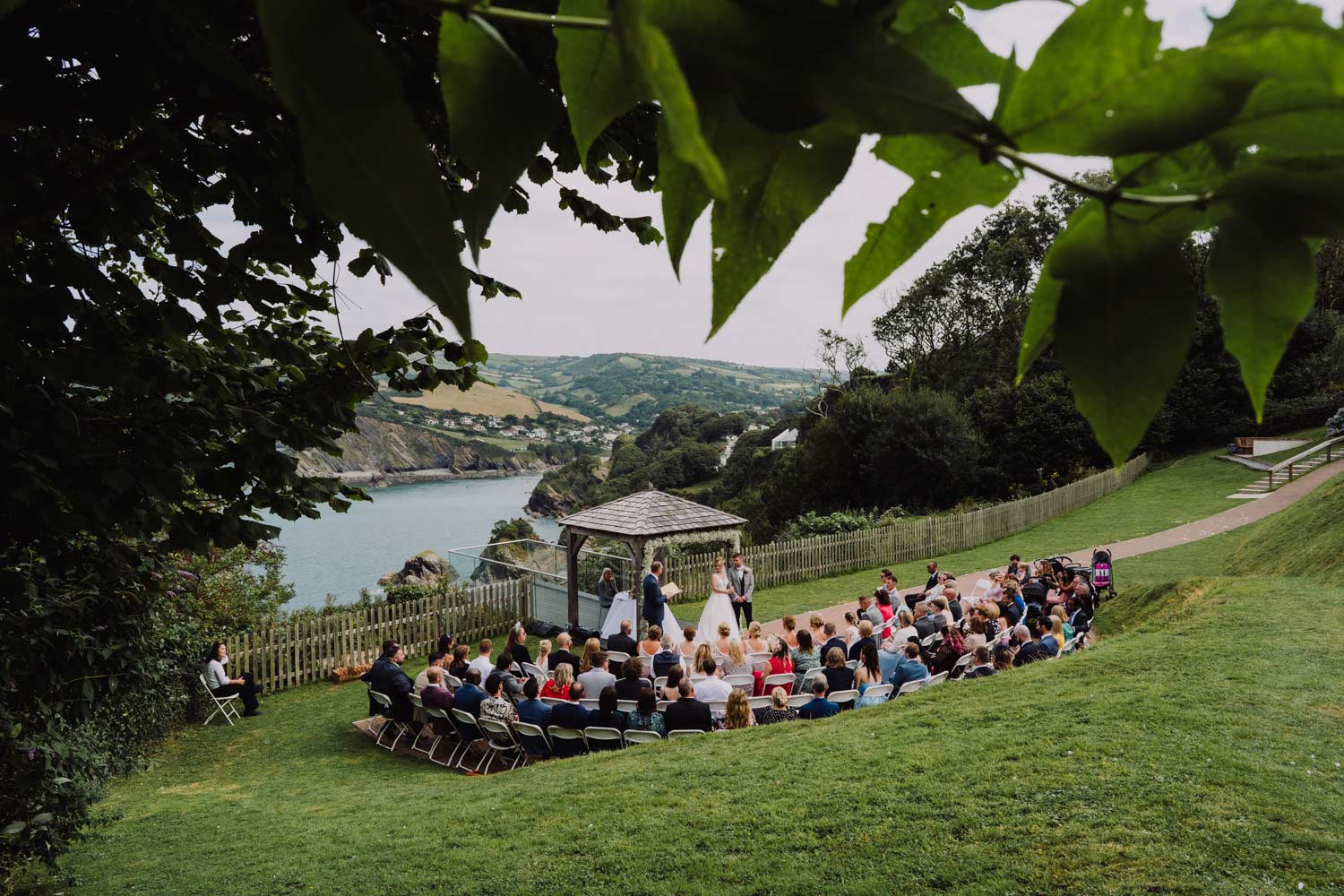 sandy cove wedding in north devon with ceremony taking place under the gazebo with the guests looking on.