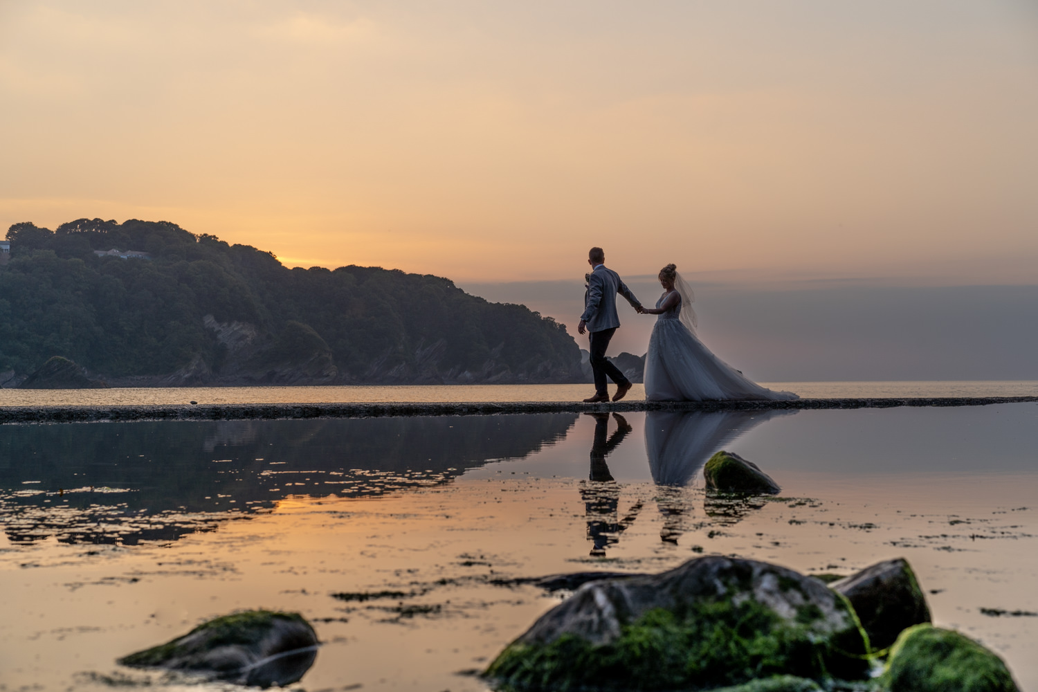 north devon coastal wedding at combe martin, bride and groom walking on coastal path with reflection in water